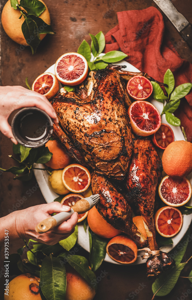 Christmas or Thanksgiving Day festive table preparation. Womans hand putting olive oil on whole roas