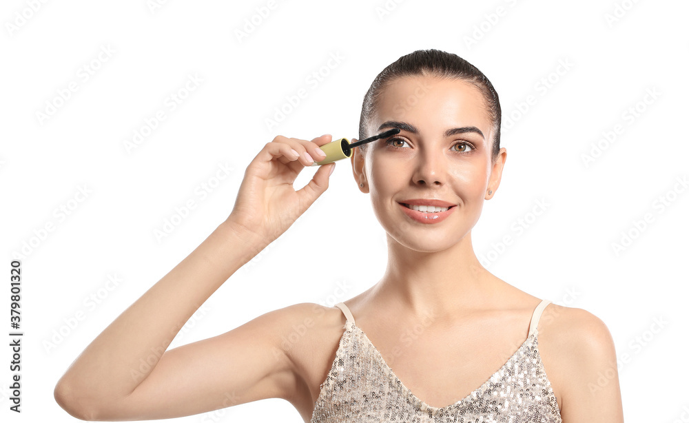 Beautiful young woman applying mascara against white background