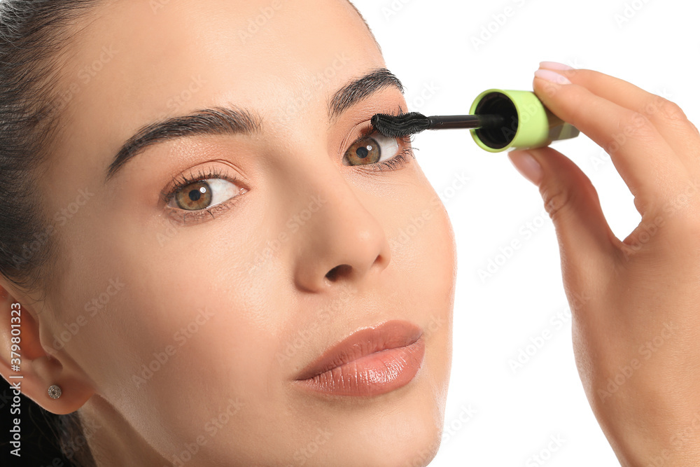 Beautiful young woman applying mascara against white background