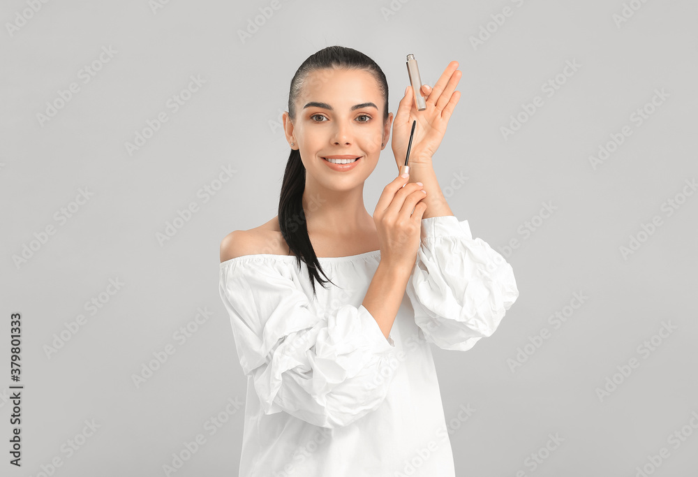 Beautiful young woman with mascara against light background