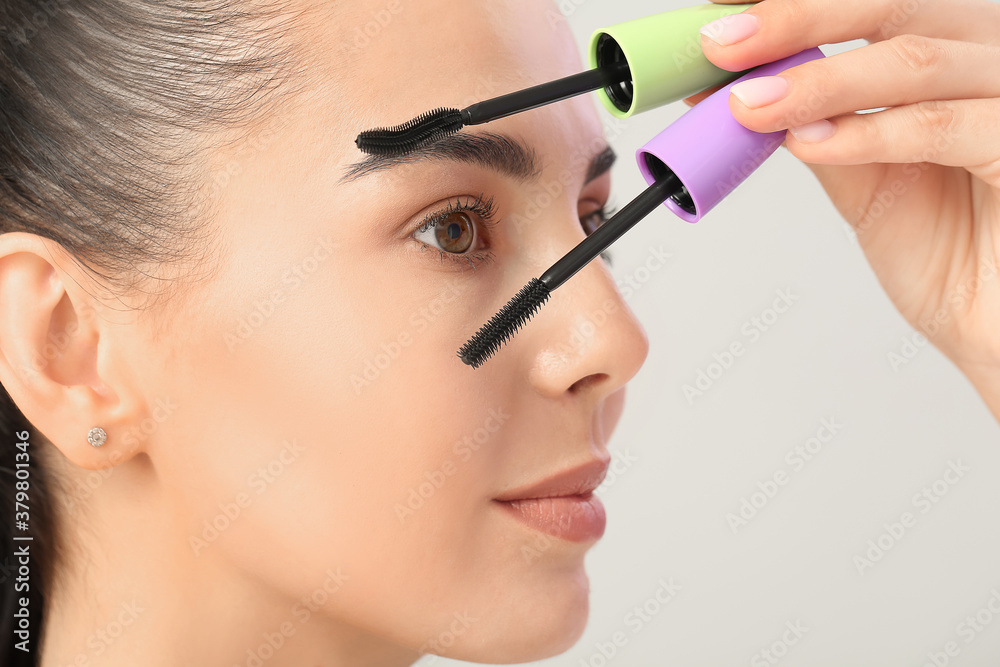 Beautiful young woman with mascara against light background