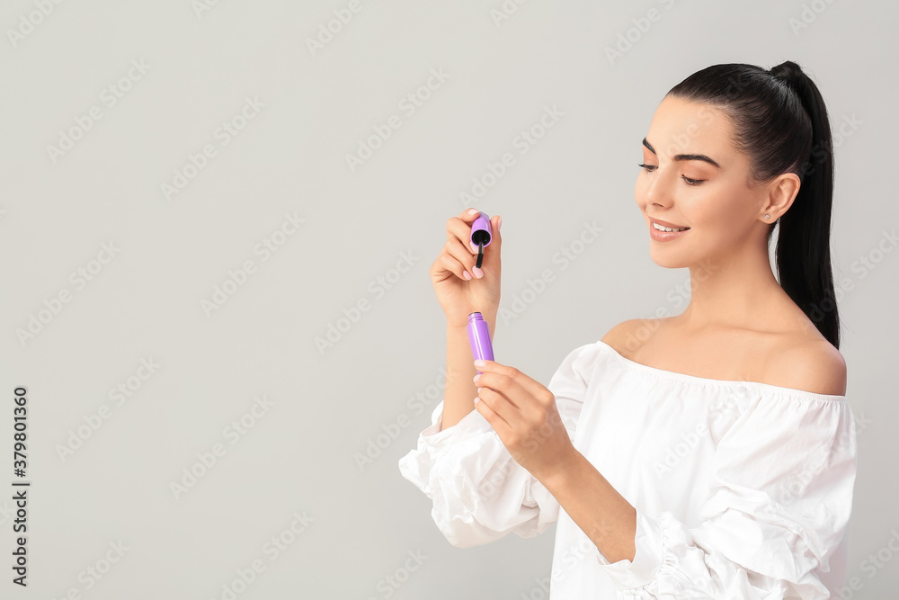 Beautiful young woman with mascara against light background