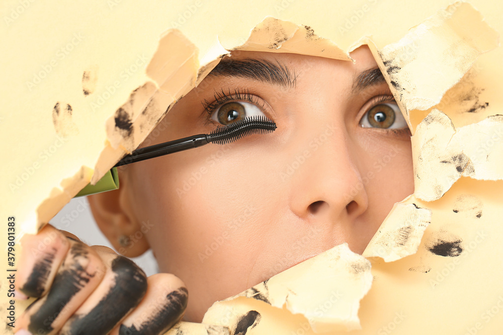 Beautiful young woman with mascara visible through hole in color paper