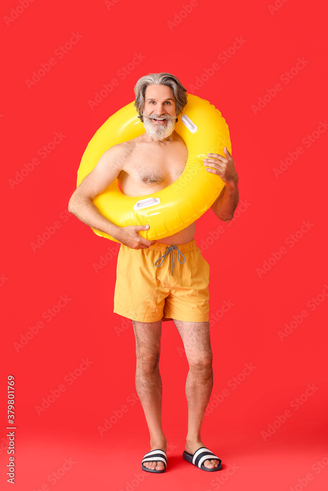 Mature man with inflatable ring on color background