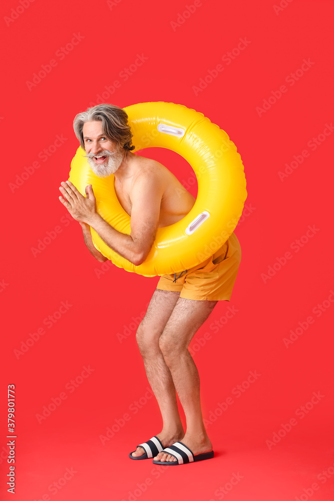 Mature man with inflatable ring on color background