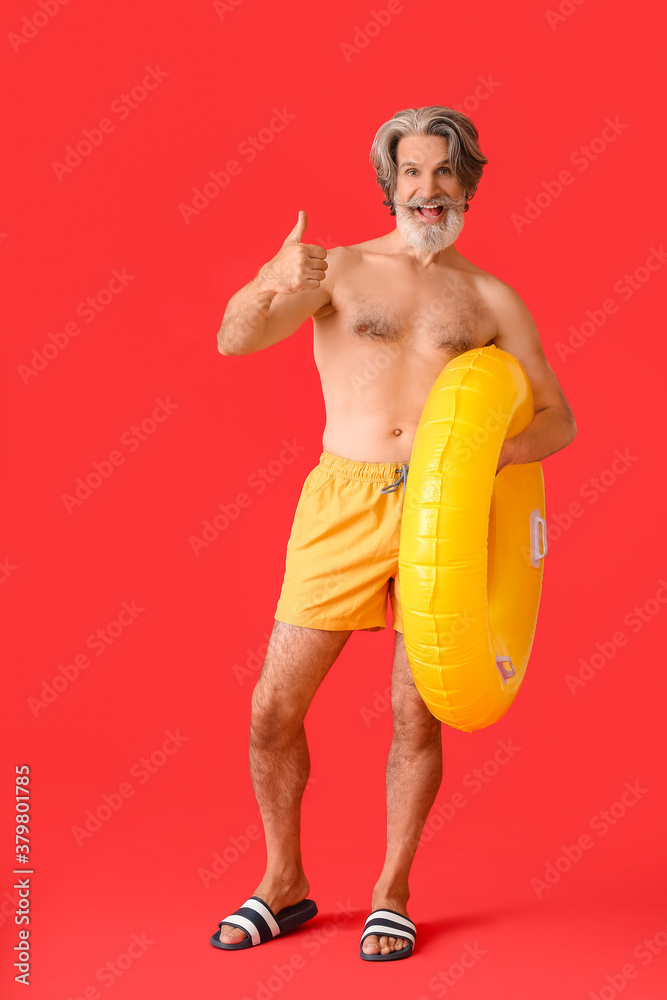 Mature man with inflatable ring showing thumb-up on color background