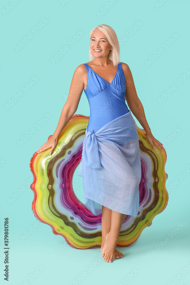 Mature woman with inflatable ring on color background