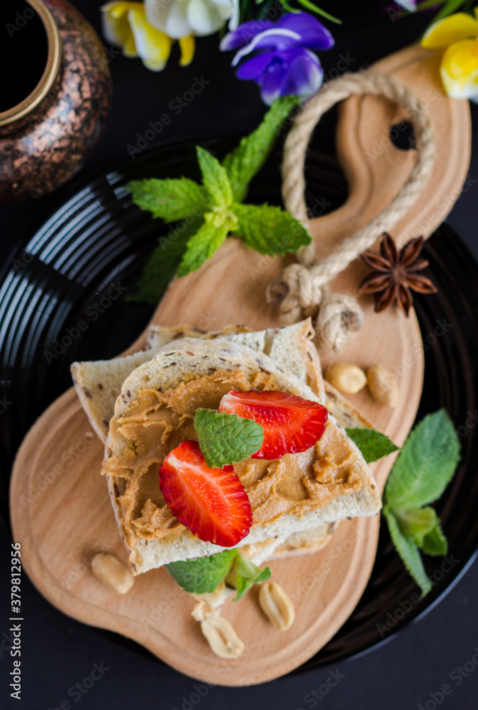 flat lay of peanut butter whole grain bread on black background, top view of toast with strawberries