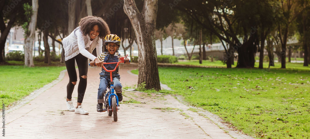 Little boy learning to ride bicycle at park with mother