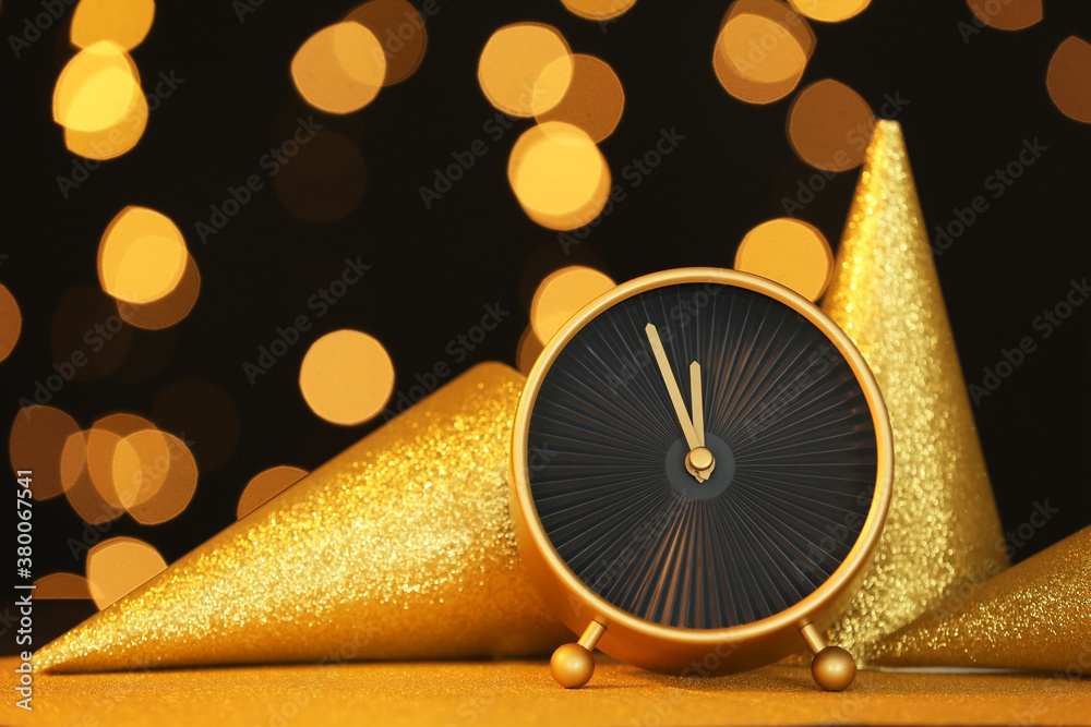 Alarm clock and party hats against blurred lights. Christmas time