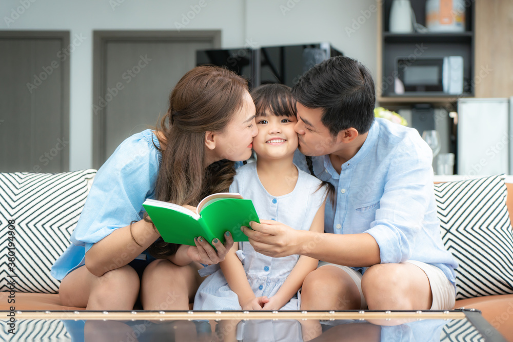 Happy Asian family with Father and Mother kiss in their daughter cheek together while sitting in liv