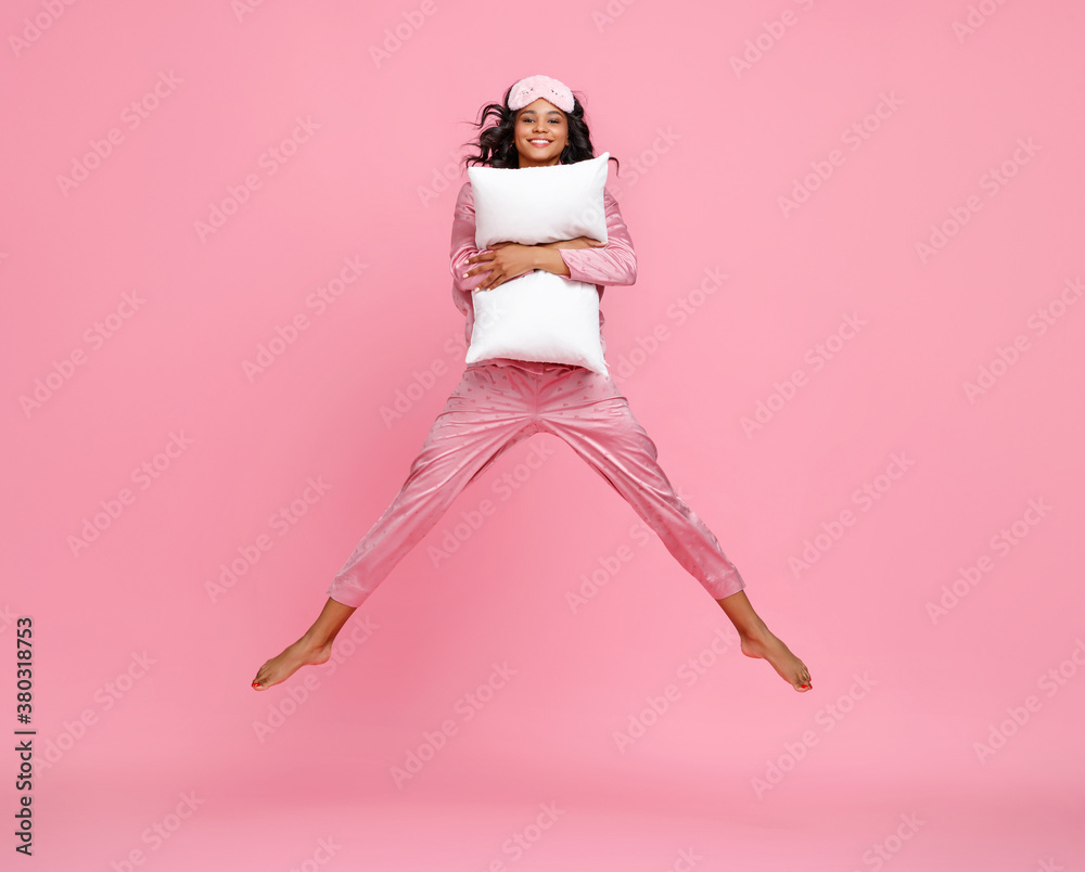 Excited woman in pajama jumping with pillow.