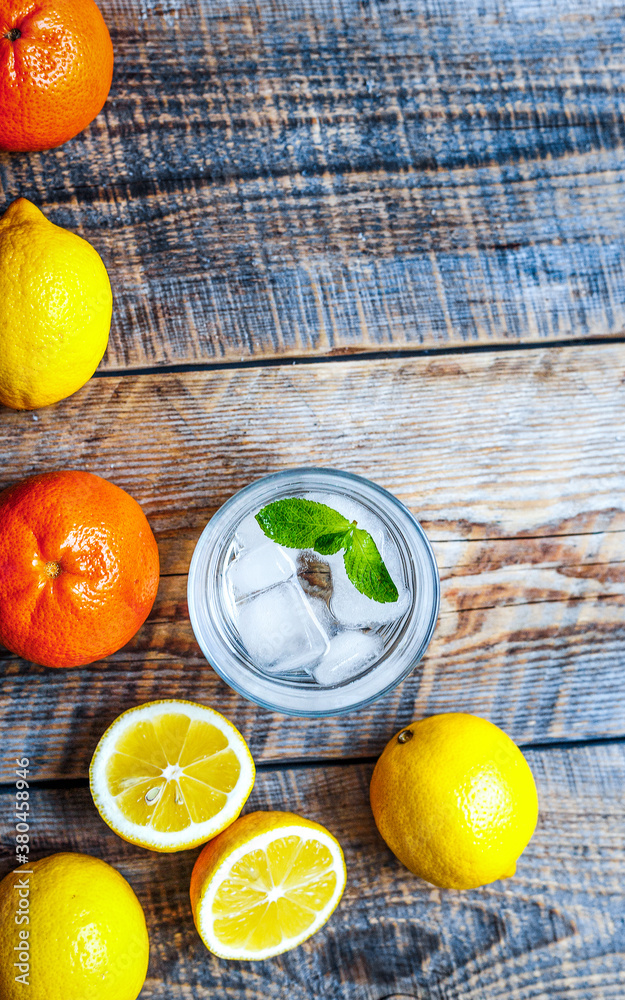 glass with ice and lemons, oranges, mint on wooden table