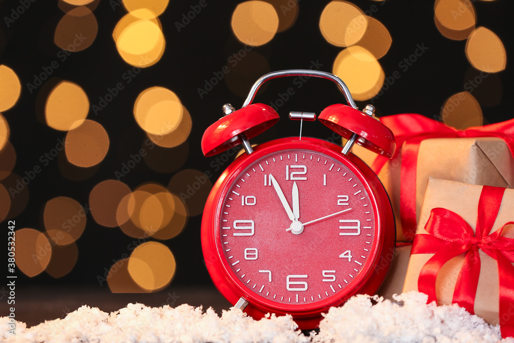 Alarm clock, snow and Christmas gifts against blurred lights