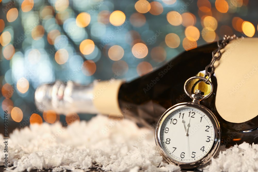 Pocket watch and bottle of champagne against blurred lights. Christmas time