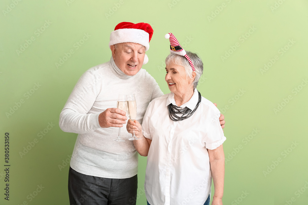 Elderly couple with champagne celebrating Christmas on color background