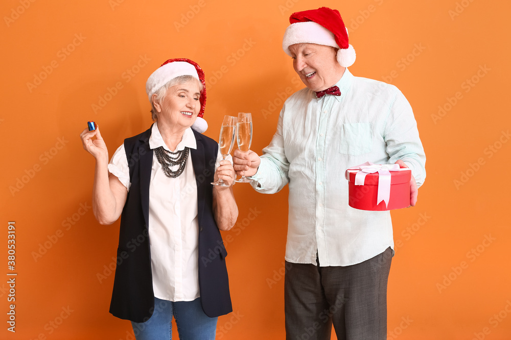 Elderly couple with champagne celebrating Christmas on color background