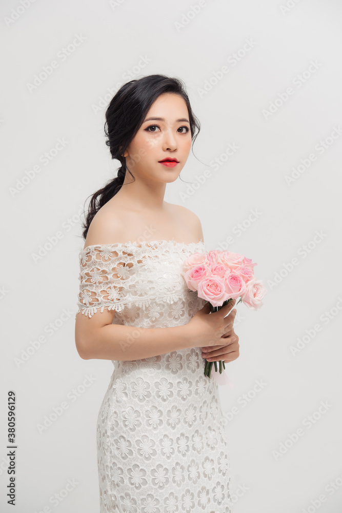 Beautiful elegant Asian young lady holding rose bouquet and wearing skinny dress over white backgrou