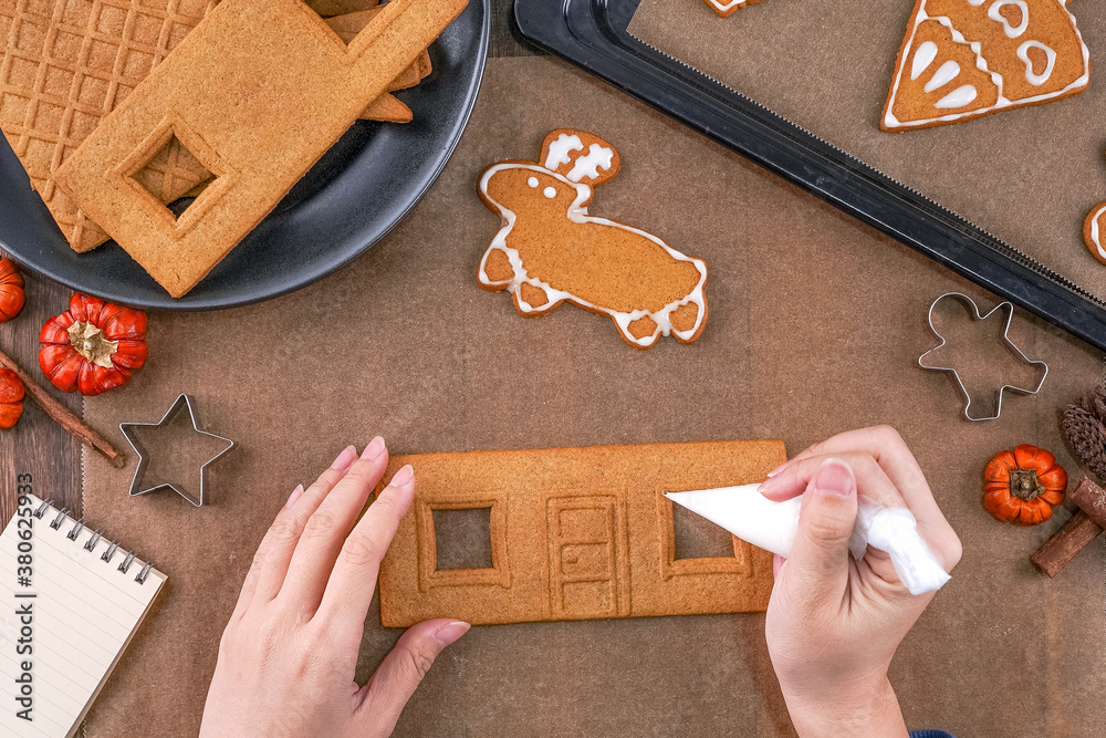 Young woman is decorating Christmas Gingerbread House cookies biscuit at home with frosting topping 