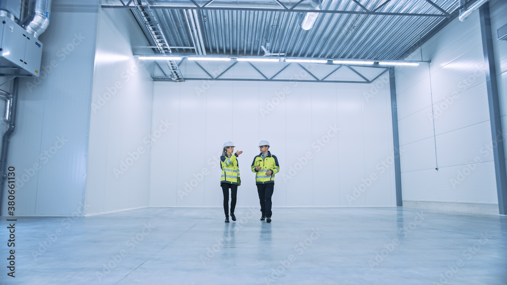 Two Engineers Talking, Walking Across Empty Factory Floor, inspecting, Planning Where All the Machin