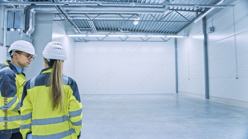 Two Engineers Talking, Standing in the Middle of an Empty Warehouse, Inspecting, Planning Future Fac