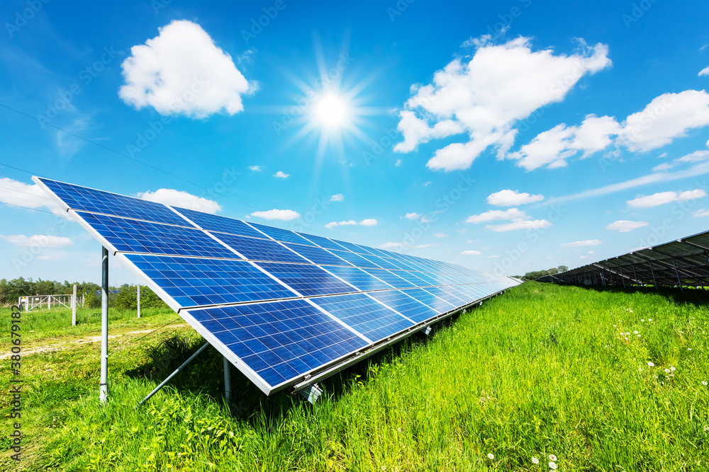 Solar panel under blue sky with sun. Green grass and cloudy sky. Alternative energy concept