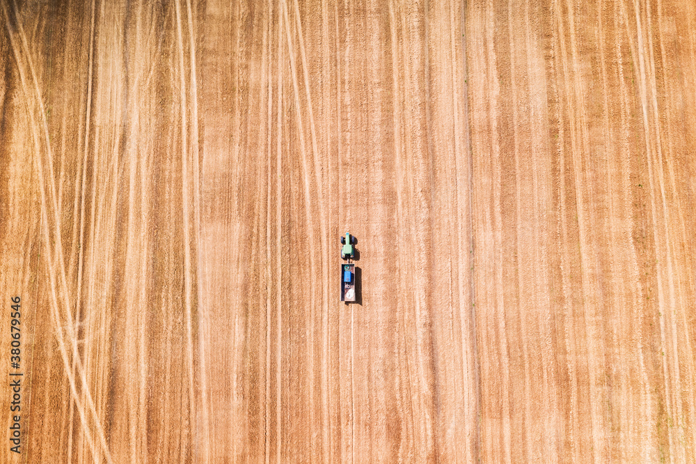 Lonely tractor in a wheat field during the harvest while waiting for the combine. Aerial top view