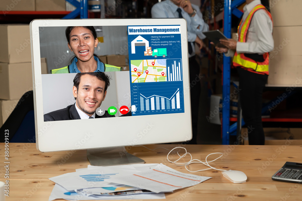 Warehouse staff talking on video call at computer screen in storage warehouse . Online software tech