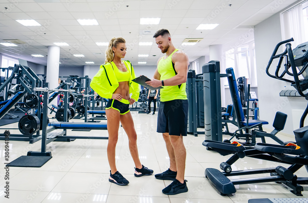 Beautiful young woman with her personal trainer at the gym discuss her progress on a clipboard held 