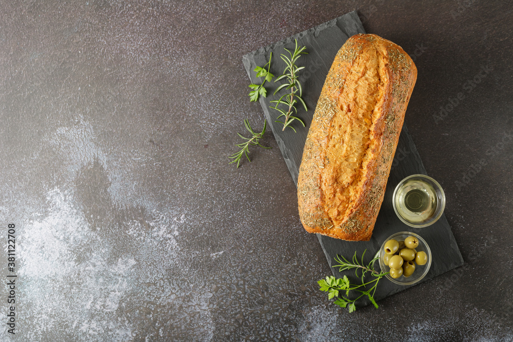 Fresh baked italian Ciabatta with herbs, spices and olives on stone board.