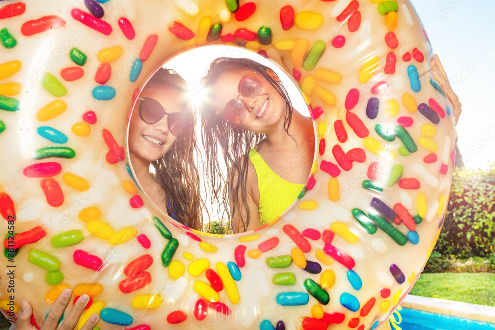 Two girls 16 years old smile looking out from inside inflatable doughnut wearing sunglasses