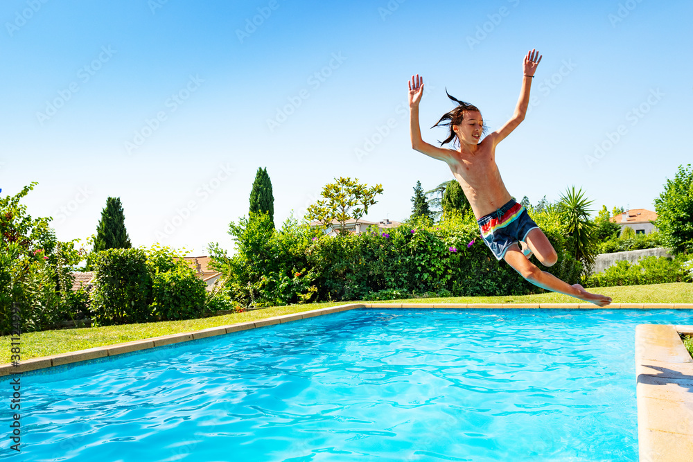 Teenage boy jump in mid air into the swimming pool view from side scream and smile with hands up in 