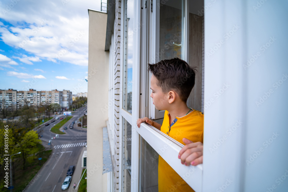 Young thoughtful teenage boy is standing on a balcony and thinking about life.