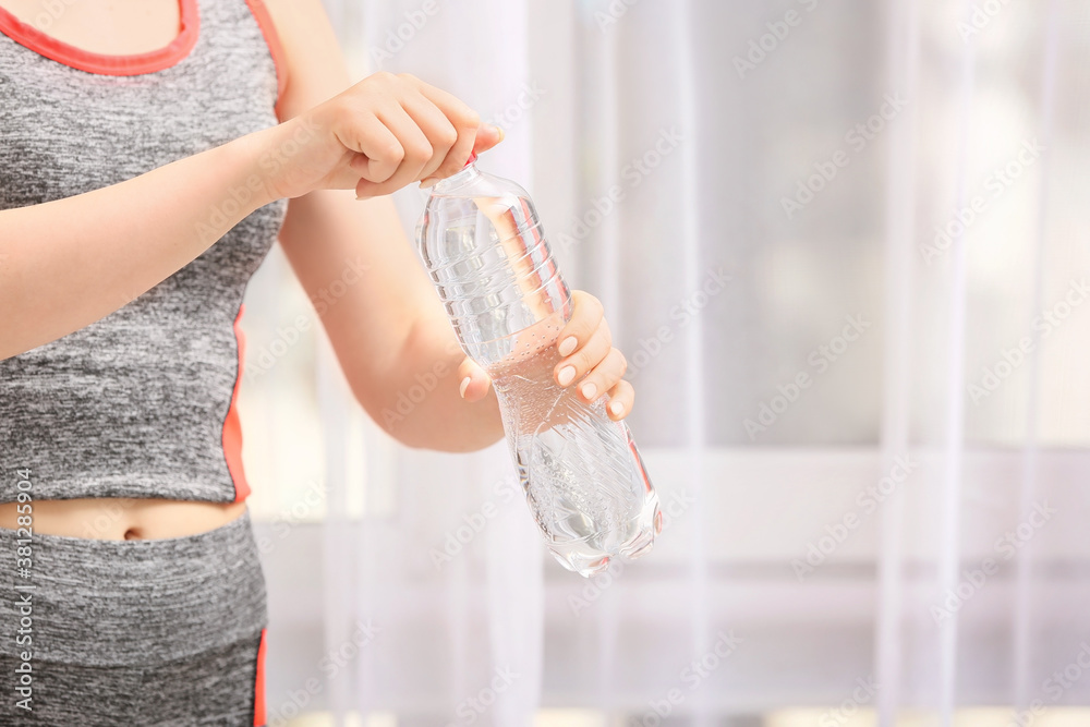 Sportswoman with bottle of fresh water indoors