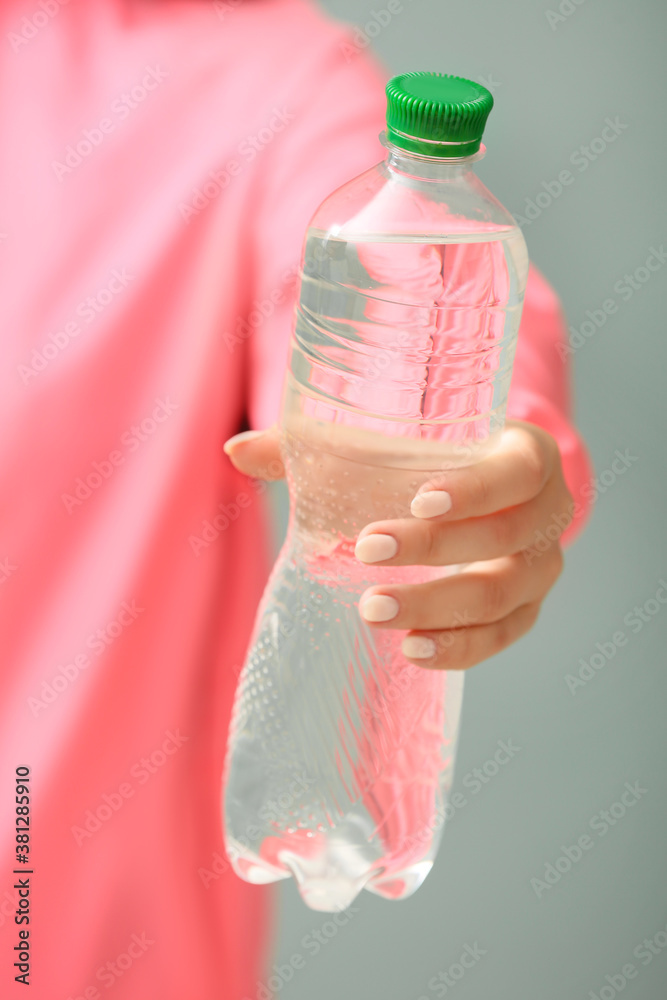 Sportswoman with bottle of fresh water on color background, closeup