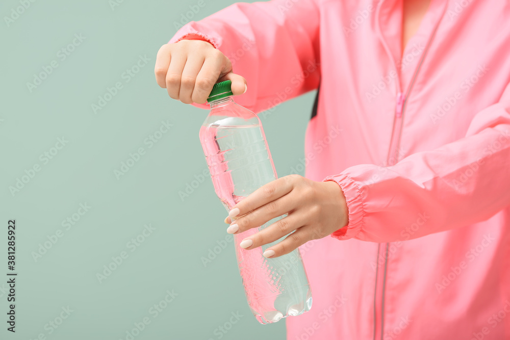 Sportswoman with bottle of fresh water on color background, closeup