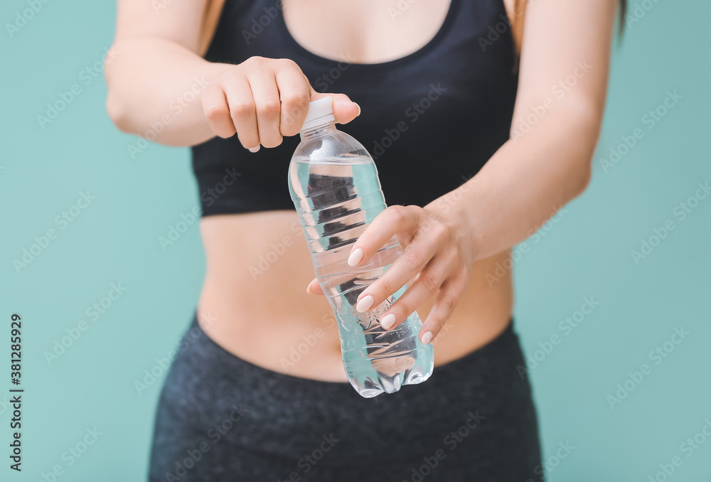 Sportswoman with bottle of fresh water on color background, closeup