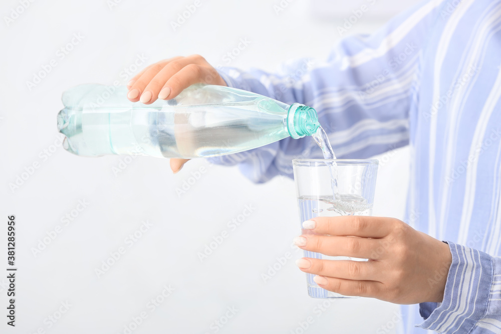 Woman pouring water from bottle into glass on light background