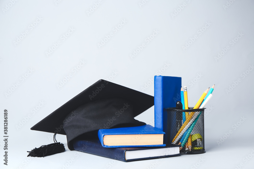 Graduation hat, stationery and books on light background