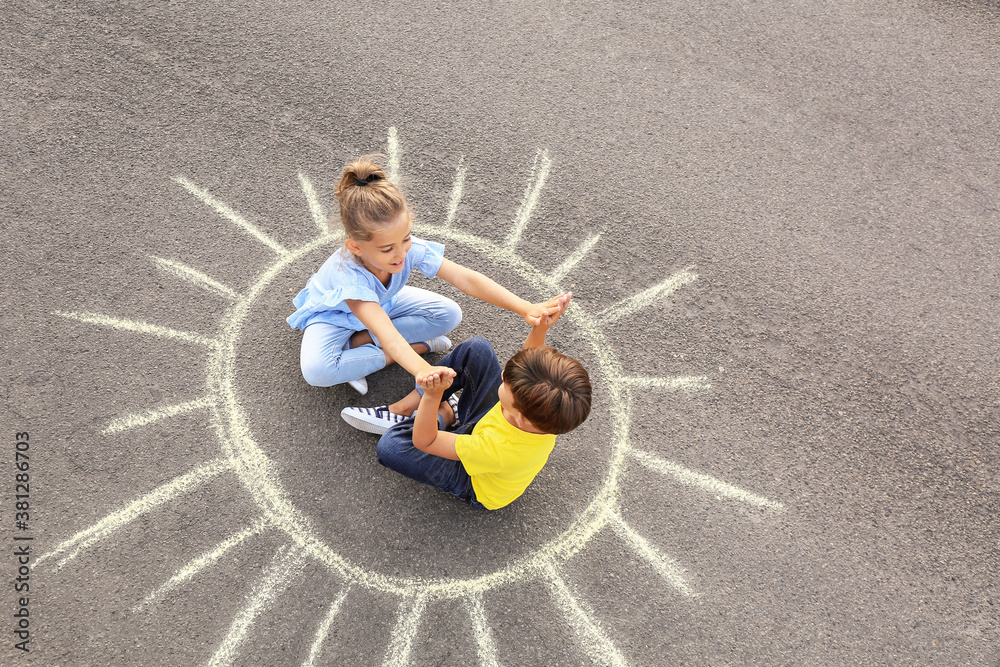 Little children sitting on chalk drawing of sun outdoors