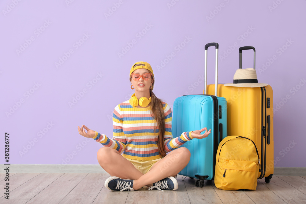 Young woman with luggage meditating near color wall. Travel concept