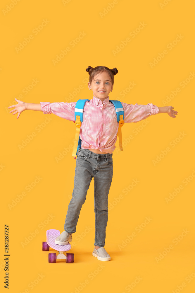 Little schoolgirl with skateboard on color background