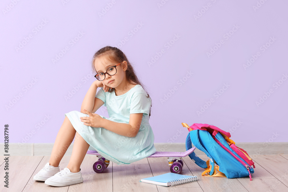 Little schoolgirl sitting on skateboard near color wall