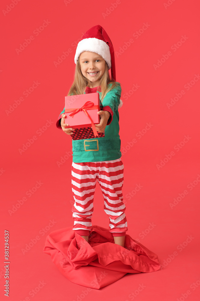 Cute little girl dressed as elf and with Christmas gift on color background