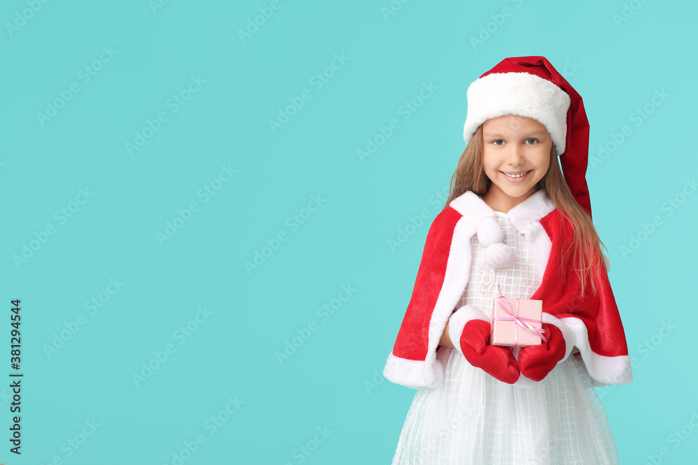 Cute little girl in Santa Claus costume and with Christmas gift on color background