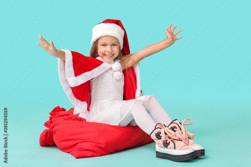 Cute little girl in Santa Claus costume and with Christmas bag on color background