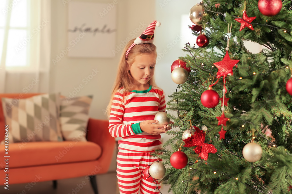 Cute little girl decorating Christmas tree at home