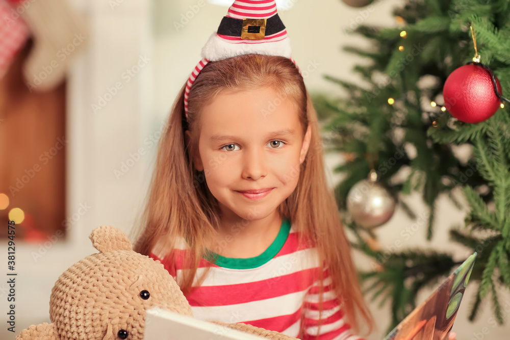 Cute little girl reading book at home on Christmas eve