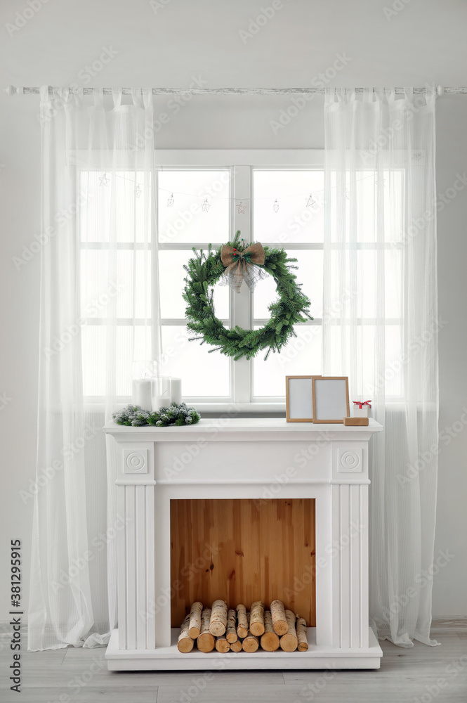 Beautiful Christmas wreath hanging on window near fireplace in room