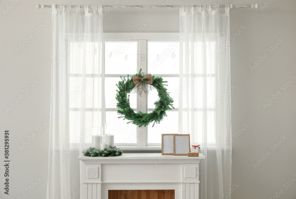 Beautiful Christmas wreath hanging on window near fireplace in room